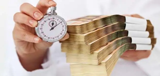 يد تحمل ساعة توقيت ونقودًا